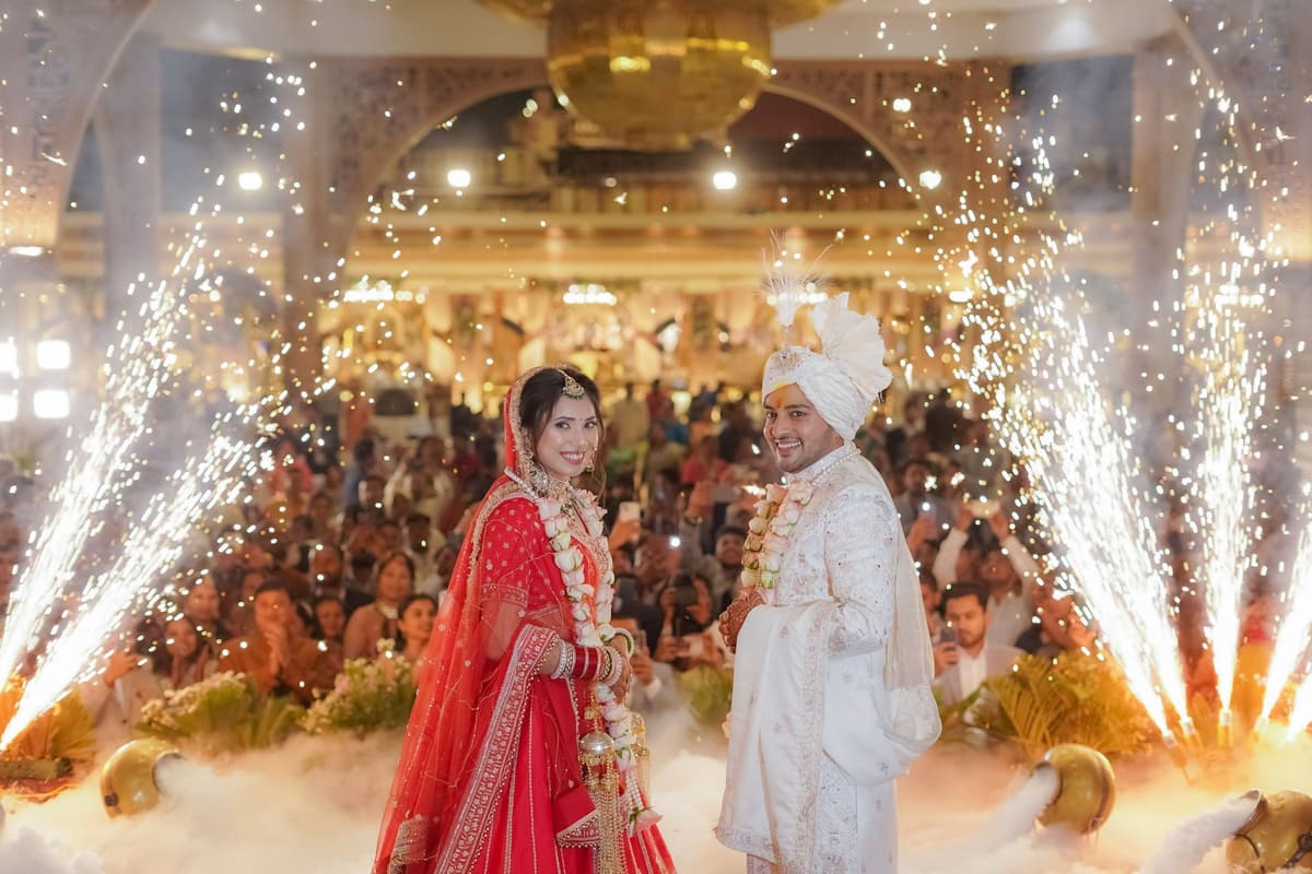 The couple stand on a stage in a packed hall, low fog at their feet and cold-spark fountains firing on both sides.