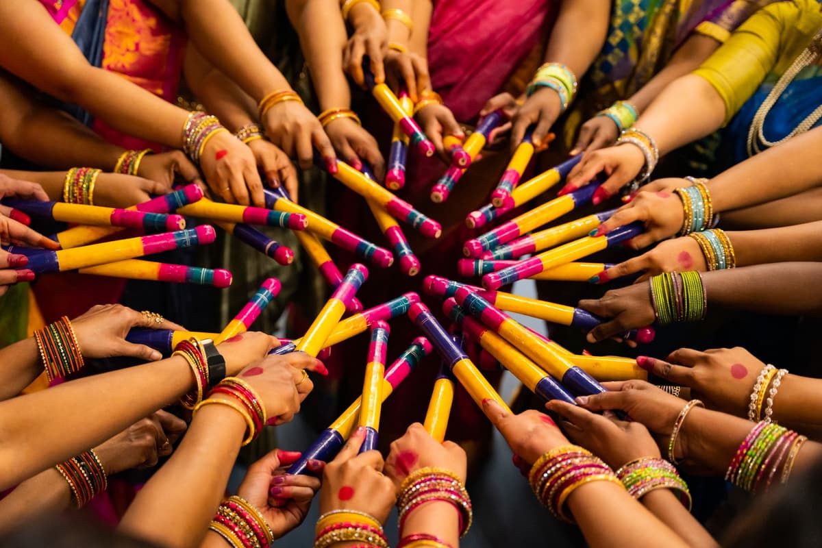 A circle of arms in bangles and bright sleeves meet in the middle, painted dandiya sticks crossing at the center.
